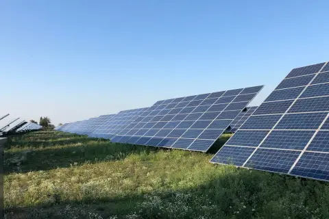 Rząd paneli fotowoltaicznych na tle błękitnego nieba. Widać, że każdy panel jest zamontowany na trackerze, który pozwala na optymalne ustawienie względem słońca.