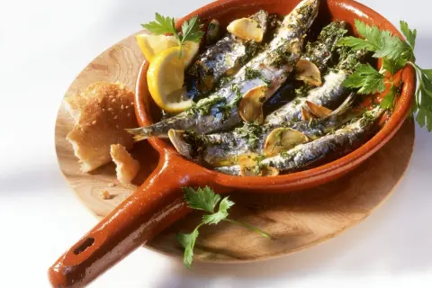 Leckeres Sardinen Rezept in einer Terracotta-Pfanne mit Zitrone, Knoblauch und Petersilie, dazu Brot.