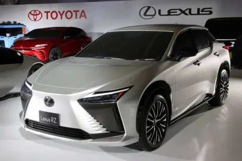 Elegancki, srebrny Lexus RZ prezentuje się na tle logo Toyoty i Lexusa.