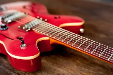 Czerwona gitara elektryczna leży na drewnianym blacie. Idealny instrument, by zacząć przygodę i nauczyć się grać na gitarze elektrycznej.