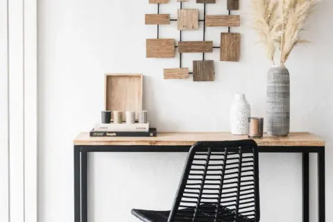 Un bureau en bois avec une chaise noire, des livres, des vases et une décoration murale. Idéal pour apprendre comment décalquer sur du bois.