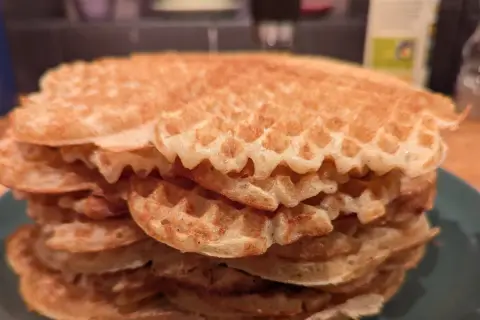 En hög med gyllene, glutenfria våfflor på en grön tallrik. Perfekt för en frukost eller fika.