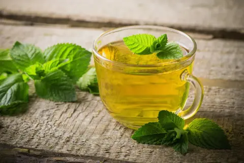 Une tasse de thé à la menthe, aux vertus et méfaits discutés, sur fond de bois vieilli.