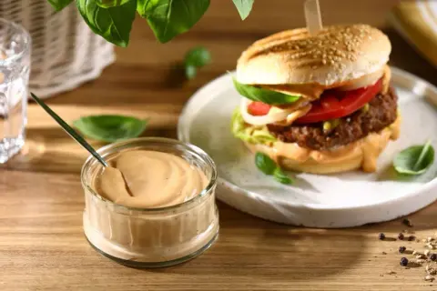 Pyszny sos do burgera w słoiczku, obok apetycznego burgera z dodatkami. Idealny do każdej kanapki.