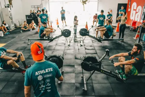 Ludzie trenują na wioślarzach w sali treningowej. Szukasz crossfit Warszawa gdzie? To miejsce jest idealne!