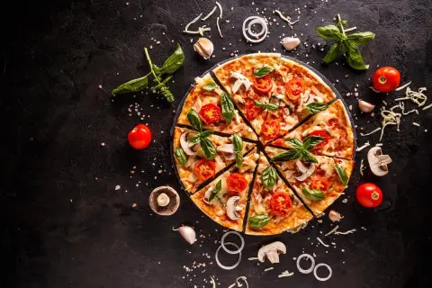 Krojona pizza z pomidorami, pieczarkami i bazylią na czarnym tle, otoczona składnikami.