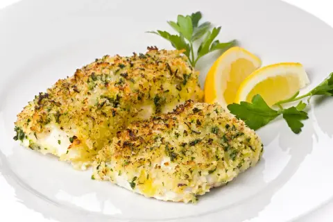 Delizioso merluzzo al forno con crosta dorata di pangrattato ed erbe aromatiche, guarnito con spicchi di limone e prezzemolo fresco.