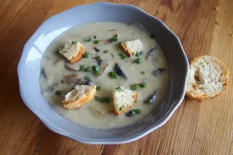 Un réconfortant velouté de champignon, garni de croûtons dorés et de ciboulette fraîche, servi dans un bol bleu sur une table en bois.