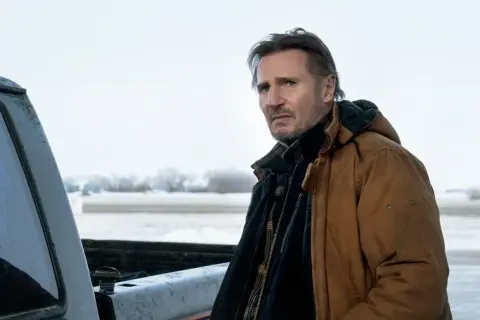 Liam Neeson w brązowej kurtce, w zimowej scenerii, jak w jego filmach.