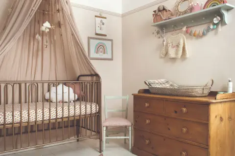 A serene modern nursery theme with a gold crib, cloud mobile, and rainbow art. A vintage dresser holds a woven basket, completing the cozy, dreamy atmosphere.