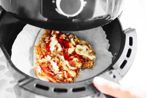 Odgrzewanie pizzy w piekarniku beztłuszczowym. Kawałek pizzy z kurczakiem, serem i sosami w koszu frytkownicy.