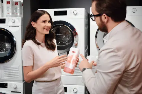 Kobieta i mężczyzna rozmawiają o produktach do prania Miele, stojąc przed nowoczesnymi pralkami.