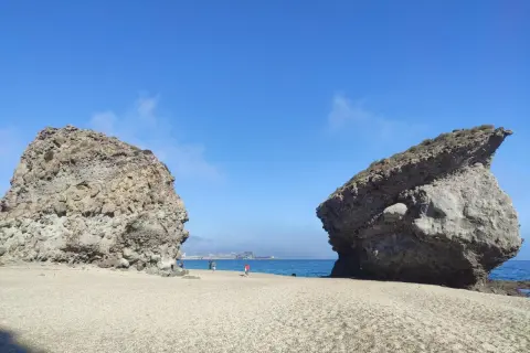 Dos rocas gigantes flanquean una playa de guijarros en la carbonera de Almería, con el mar azul y el cielo despejado de fondo.