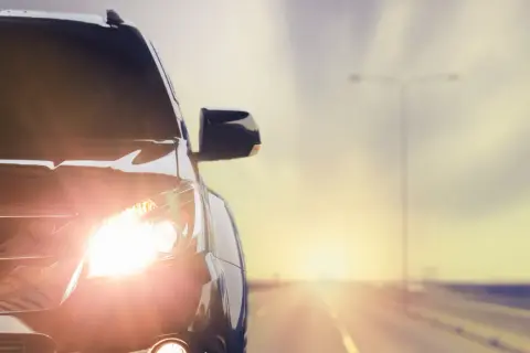 Las luces del coche brillan intensamente al amanecer en una carretera desierta.