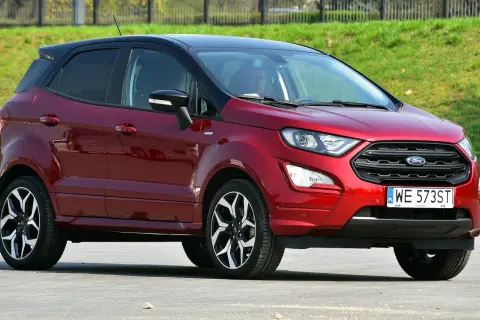 Czerwony Ford Ecosport benzyna z czarnym dachem, zaparkowany na tle zielonego zbocza.