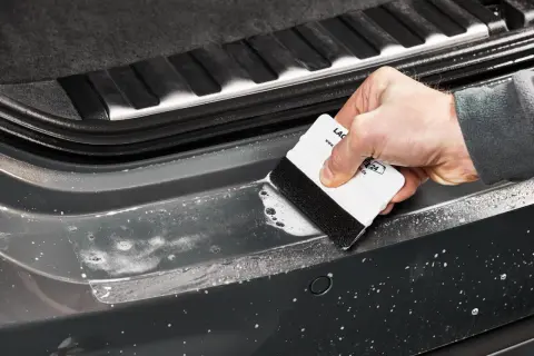 Mit der Rakeltechnik Anleitung wird die Folie blasenfrei angebracht. Ein weißer Rakel mit schwarzem Filzrand gleitet über die nasse Oberfläche des Autos.