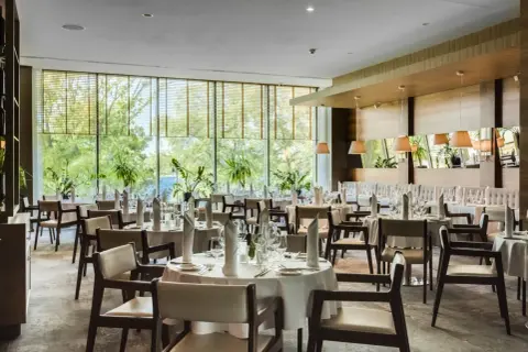 Elegancka sala restauracyjna Grand Hotel Tiffi w Iławie, z widokiem na zieleń. Stoły nakryte do posiłku, gotowe na przyjęcie gości.
