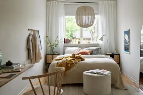 Acogedora cama bajo ventana, con manta amarilla y cojines. Ideas para un dormitorio luminoso y funcional.
