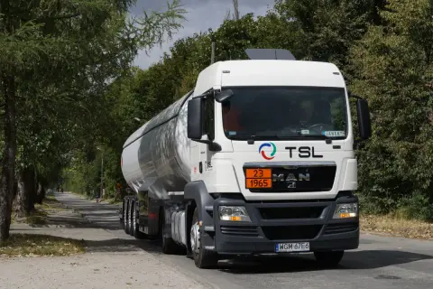 Biały cysterna z logo TSL jedzie drogą wśród drzew. To ważny element branży TSL, transportującej towary.