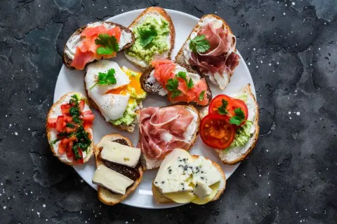 Talerz pełen pysznych sznytek: z łososiem, awokado, jajkiem w koszulce, szynką parmeńską, pomidorami i serami.