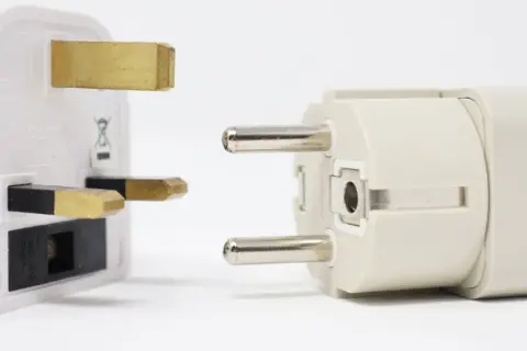Adapter do gniazdek w Hiszpanii. Biały adapter z bolcami brytyjskimi obok jasnoszarego z bolcami europejskimi.