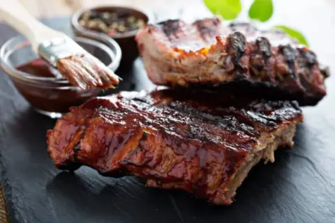 Saftige Rippchen, glasiert mit BBQ-Sauce. Ein Pinsel taucht in die Sauce, bereit für die Zubereitung: low and slow.