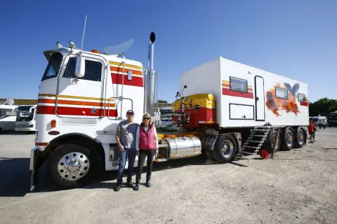 Un couple pose devant un camion américain customisé, avec une remorque aménagée en camping-car ornée d'un aigle et d'un paysage désertique.