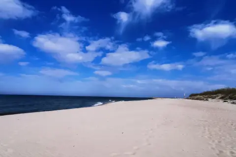 Pusta piaszczysta plaża nad Bałtykiem, błękitne niebo z chmurami, morze i wydmy.