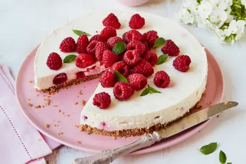 Eine köstliche Philadelphia Torte Himbeer, üppig garniert mit frischen Himbeeren und Minze, auf einem rosa Teller.