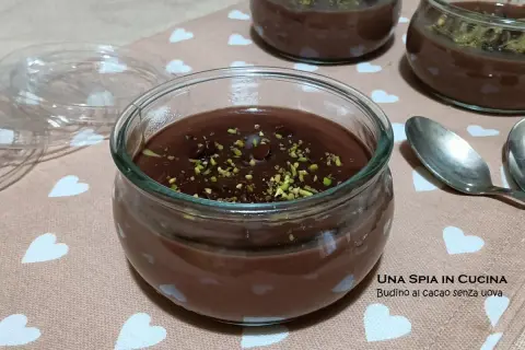 Budino al cioccolato fatto in casa, guarnito con pistacchi tritati, servito in vasetti di vetro su un tovagliolo con cuoricini.