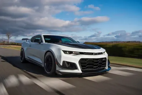 Białe Camaro ZL1 z czarną maską i spoilerem pędzi po torze wyścigowym, zostawiając za sobą rozmyte tło.