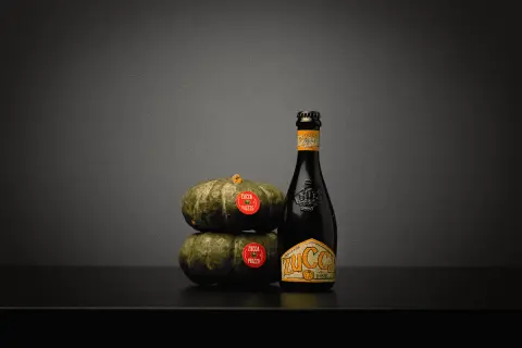 Una bottiglia di birra alla zucca accanto a due zucche impilate.