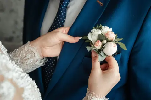 Les mains de Caroline ajustent la boutonnière sur le costume bleu du marié. Un moment tendre avant leur mariage à l'hôtel.