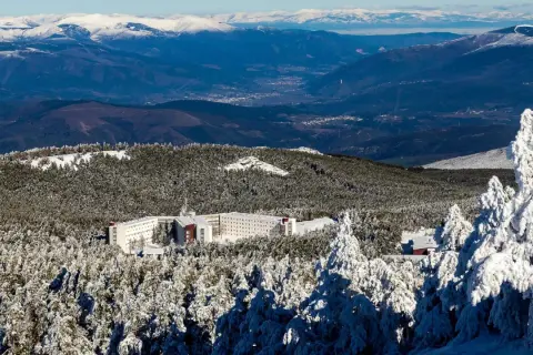 Edificio hotelero en la cabeza de Manzaneda, rodeado de pinos nevados y montañas al fondo.