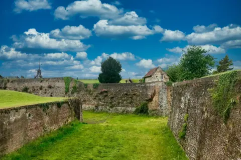 Murs de pierre et de brique du château de Montreuil, envahis par la végétation, sous un ciel bleu et nuageux.