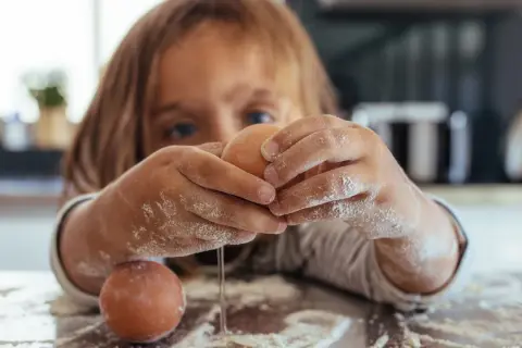 Kind mit bemehlten Händen knackt Eier. Vorsicht vor salmonellen eiern, besonders bei rohem Verzehr.