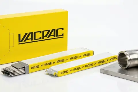 Żółte pudełko z logo VACPAC, obok opakowania z elektrodami spawalniczymi i metalowym kolankiem.