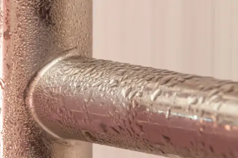 Krople wody na metalowych rurach, efekt pocenia się rur zimnej wody.
