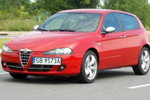 Czerwona Alfa Romeo 147 w ruchu, z widocznymi reflektorami i grillem.