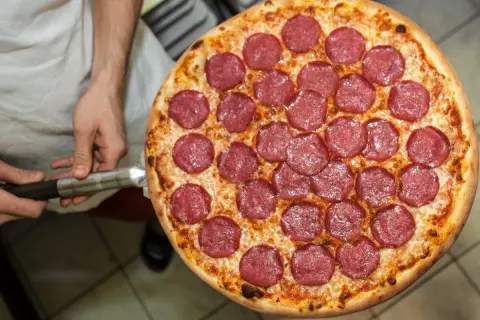 Pizza z salami na łopacie, trzymana przez kucharza.