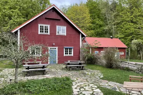 Stocklycke vandrarhem, röda trähus med vita knutar och fönster, omgivna av grönskande skog. Picknickbord och stenlagd uteplats inbjuder till avkoppling.