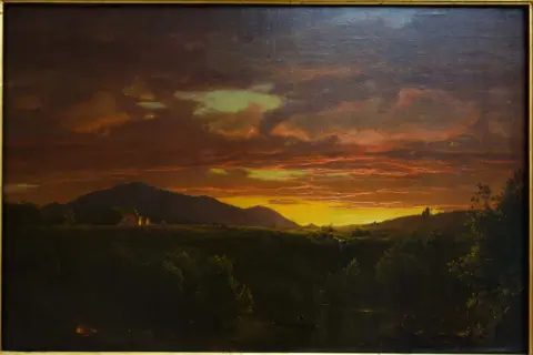 Un paysage de crépuscule, baigné de lumières orangées et dorées, évoquant la beauté mélancolique d'un crépuscule victor hugo. Des montagnes se dressent à l'horizon, tandis que des lumières douces émanent de quelques habitations.