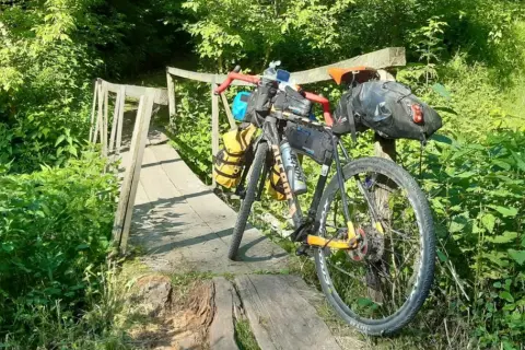 Rower wyprawowy na drewnianym moście, gotowy na mazowiecki gravel. Otoczony bujną zielenią, zaprasza do przygody.