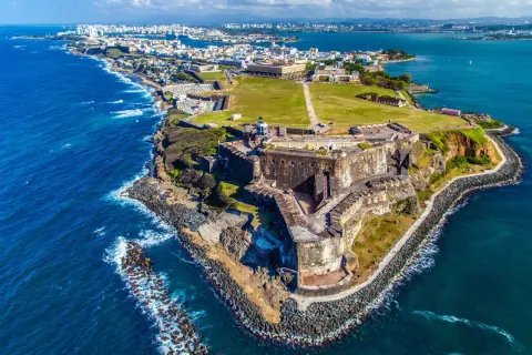 Widok na zabytkową fortecę i miasto San Juan, gdzie jest Puerto Rico. Błękitne morze otacza skaliste wybrzeże.