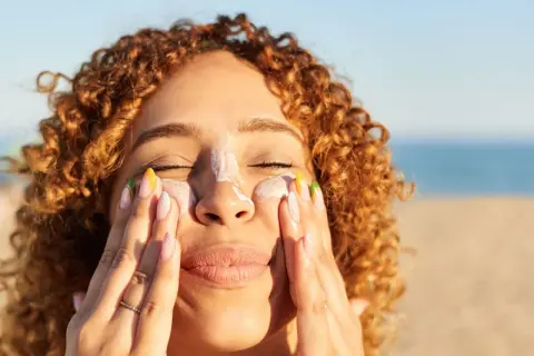 Frauenhände verteilen Sonnencreme mit Methylene bis-benzotriazolyl tetramethylbutylphenol auf der Nase.