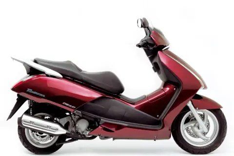 Elegancki, czerwony skuter Honda Pantheon z czarnym siedzeniem i chromowanym bagażnikiem, gotowy na miejskie przygody.