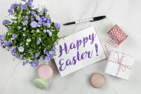 Wielkanocne słówka po angielsku: "Happy Easter!" na kartce, obok kwiatów, makaroników i prezentu.