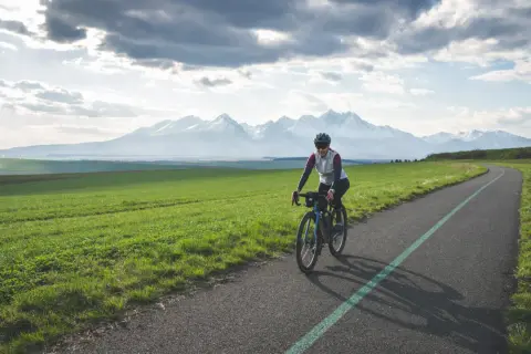 Kobieta na rowerze przemierza malowniczą trasę z widokiem na ośnieżone Tatry. To idealne miejsce na **velo tatry** i podziwianie krajobrazów.