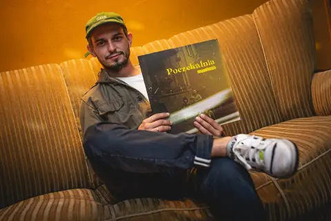 Młody mężczyzna w czapce z daszkiem siedzi na kanapie, trzymając w rękach płytę Vito Bambino "Poczekalnia".