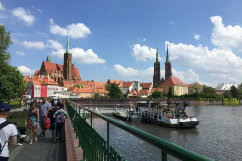 Mosty i katedra to to, z czego słynie Wrocław. Ludzie spacerują po moście, podziwiając widok na rzekę i zabytkową architekturę.
